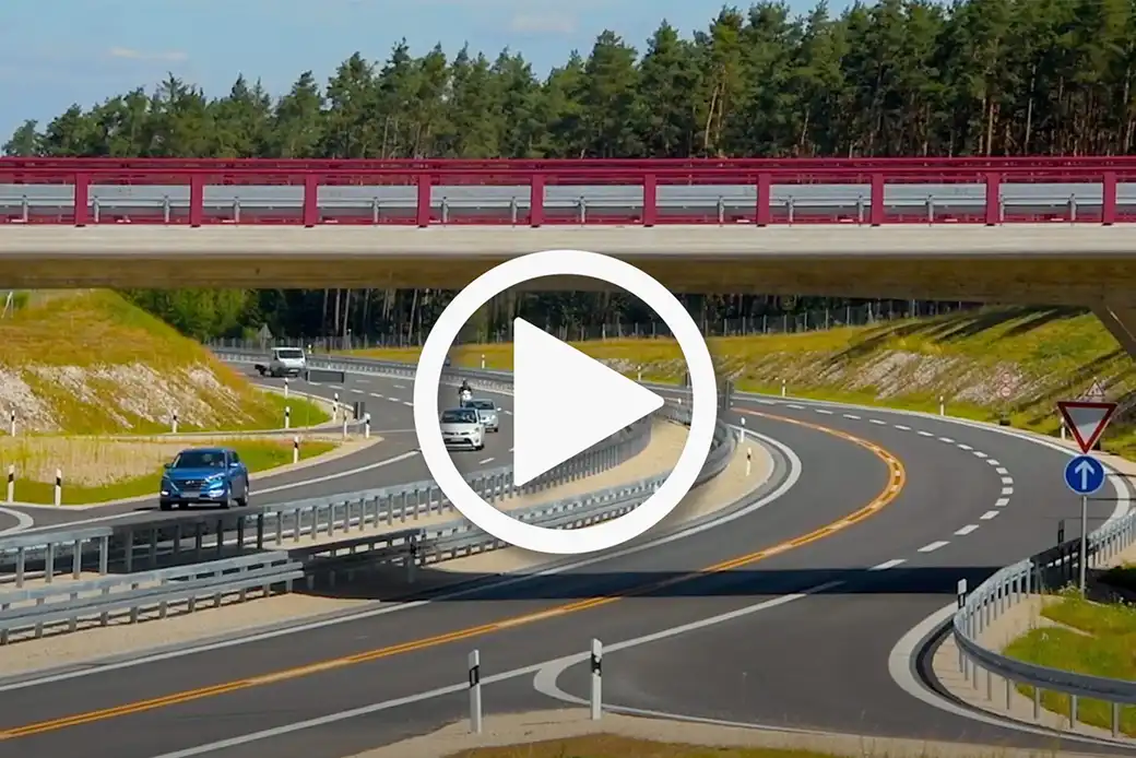 Kurvenreiche Autobahn, Autos, rote Brücke, Gras, Bäume, Vorfahrtsschild auf der rechten Seite.