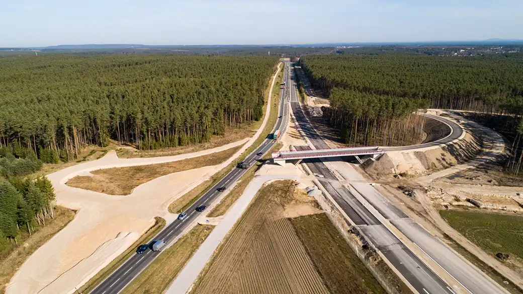 Luftaufnahme einer Autobahn mit Überführung und Fahrzeugen in einem Waldgebiet.