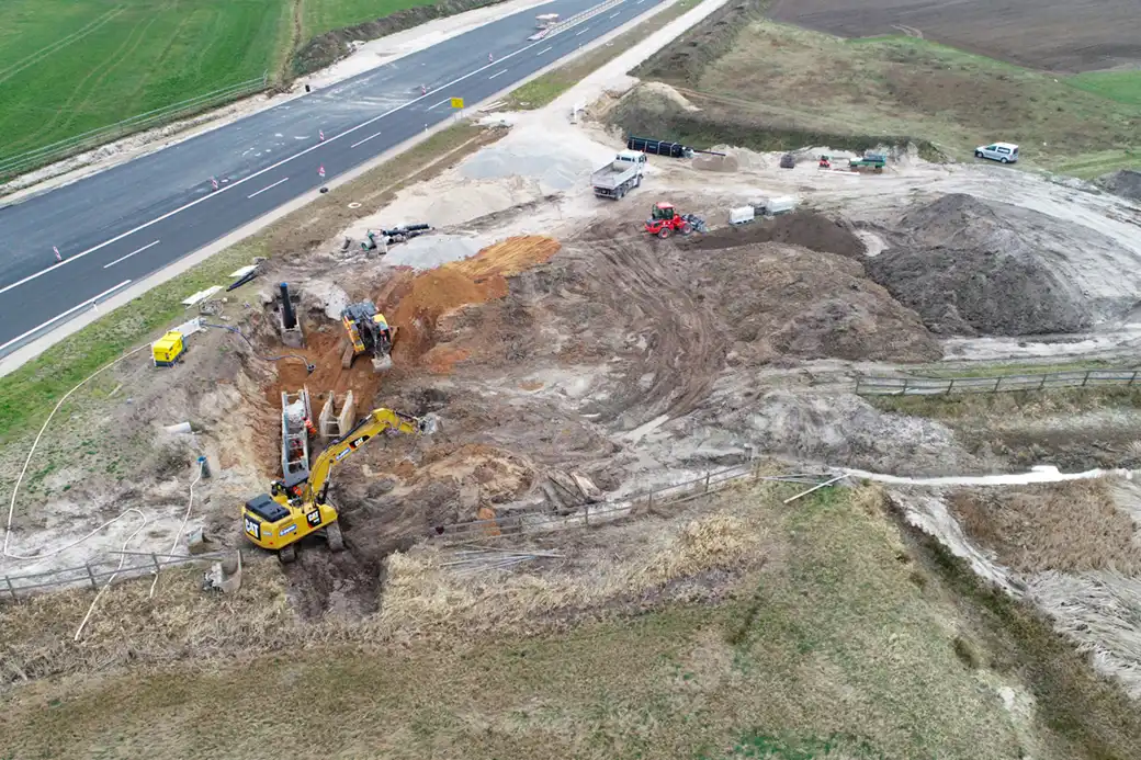 Luftaufnahme: Baustelle mit Baggern, Fahrzeugen und Geräten an der Straße.