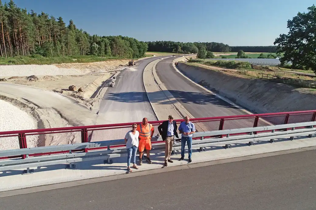 Vier Personen stehen auf einer Brücke und überblicken Straßenbau und Wald.