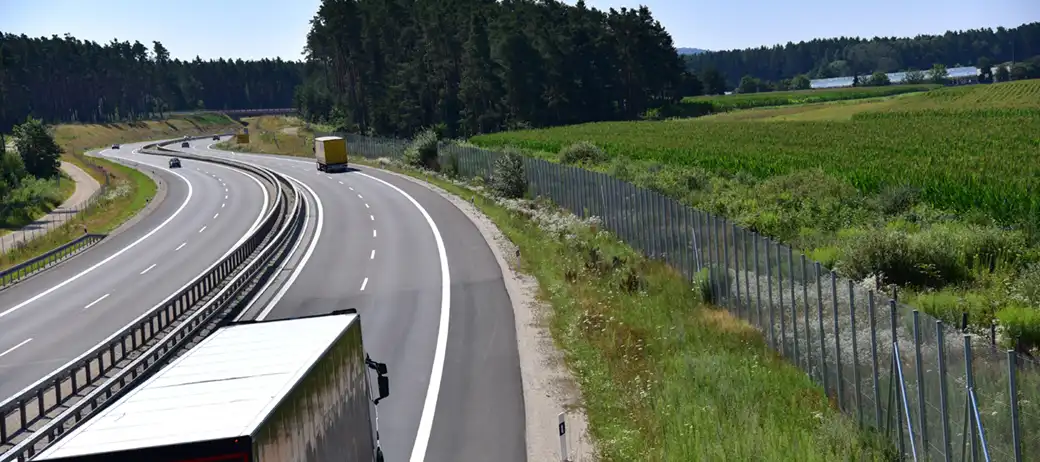 Die Fahrzeuge fahren in beide Richtungen auf einer kurvenreichen Straße, die an Feldern und Bäumen vorbeiführt.