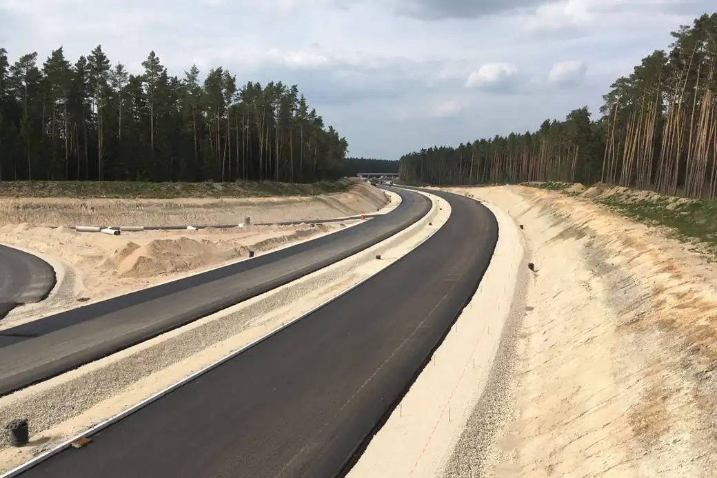 Eine neue Straße führt durch sandige Hänge und Wälder bei bewölktem Himmel.