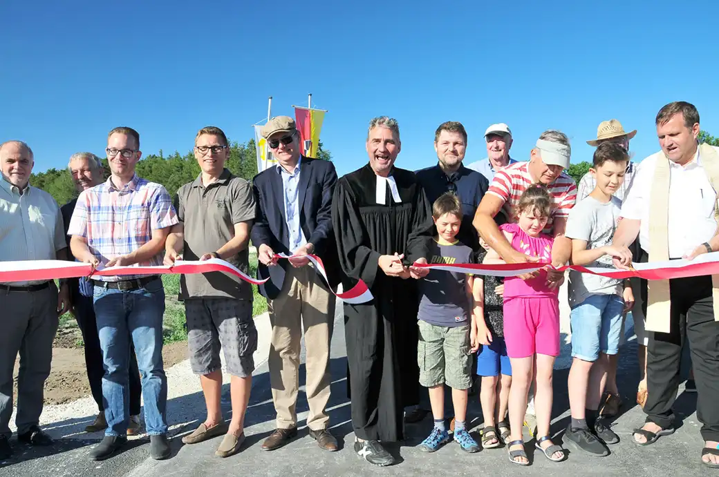 Menschen, darunter auch Kinder, durchschneiden bei einer Zeremonie im Freien ein rotes Band.