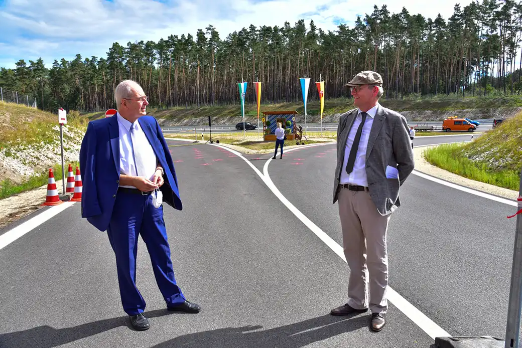 Zwei Geschäftsleute stehen auf einer neuen Straße mit Kegeln und Wald dahinter.