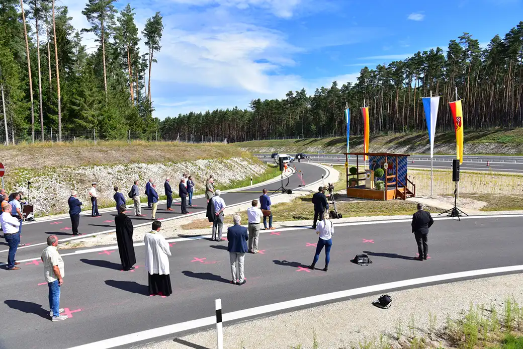 Die Menschen stehen bei der Zeremonie unter freiem Himmel in der Nähe des Podiums und der Fahnen in Abständen auf der Straße.