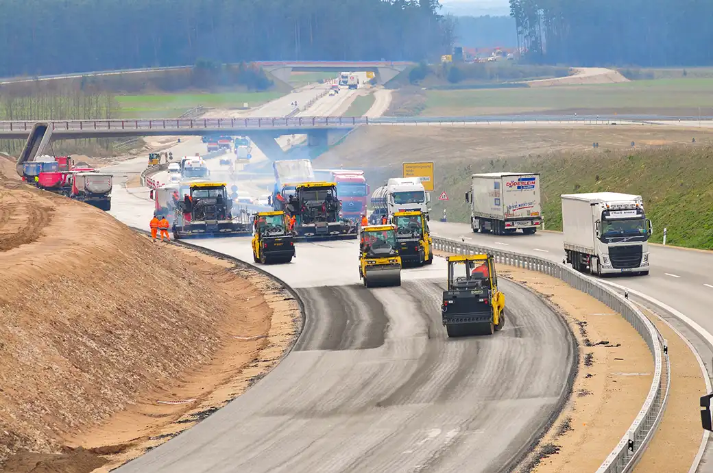 Straßenbauarbeiter legen eine neue Fahrspur an, während der Verkehr in der Nähe vorbeifließt.