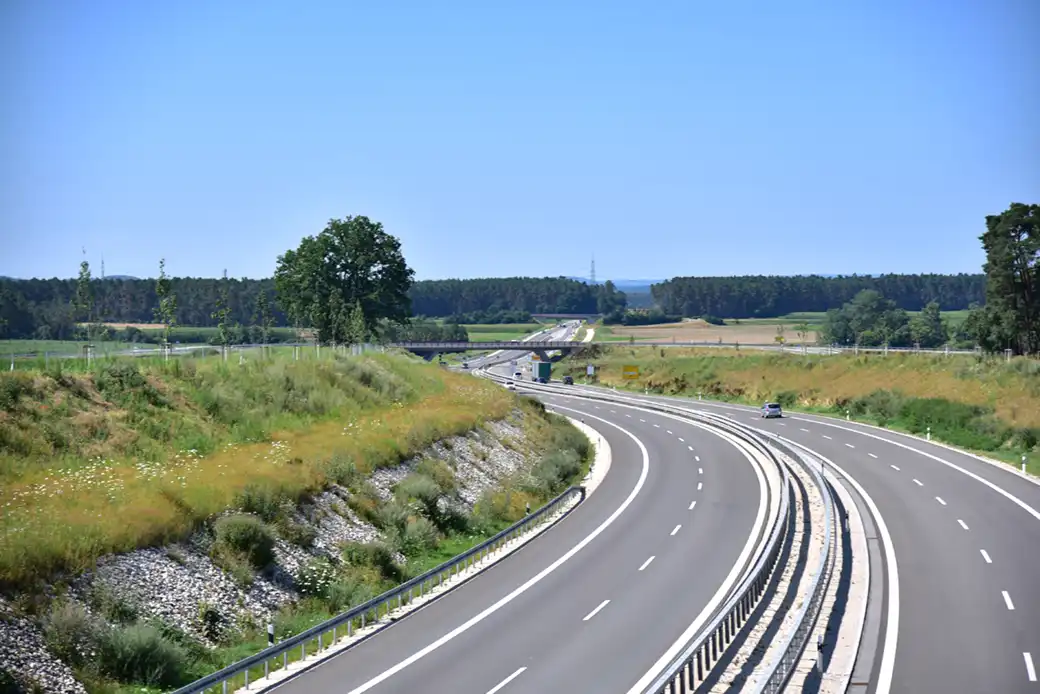 Kurvenreiche Autobahn durch grüne, ländliche Landschaft unter sonnigem, blauem Himmel.
