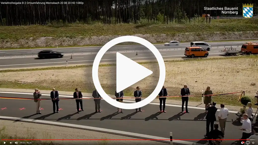 Anzüge bei der Einweihung der neuen Straße, dahinter Verkehrs- und Nutzfahrzeuge.