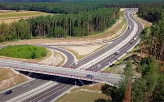 Autobahnkreuz mit Überführung, Autos, Wälder und Felder rund um die Straßen.