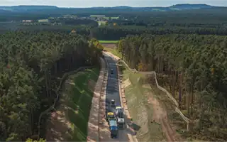 Luftaufnahme eines Straßenbaus mit Fahrzeugen in einem Waldgebiet.